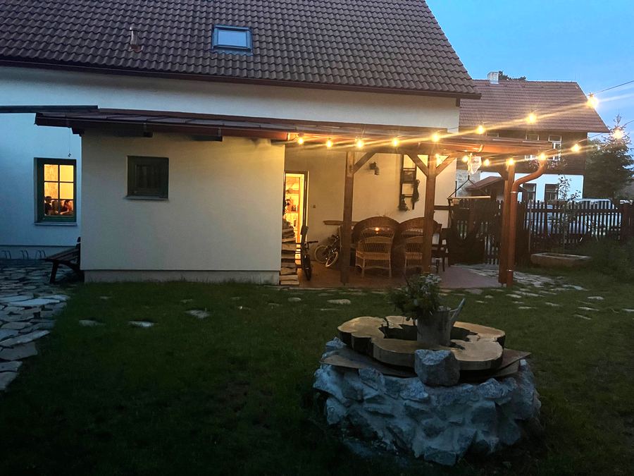 Zastřešená terasa za soumraku, nad ní svítí řetěz žárovek